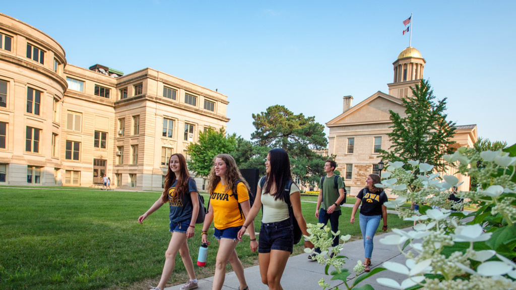 University of Iowa students walk across campus while talking on a sunny day. 
